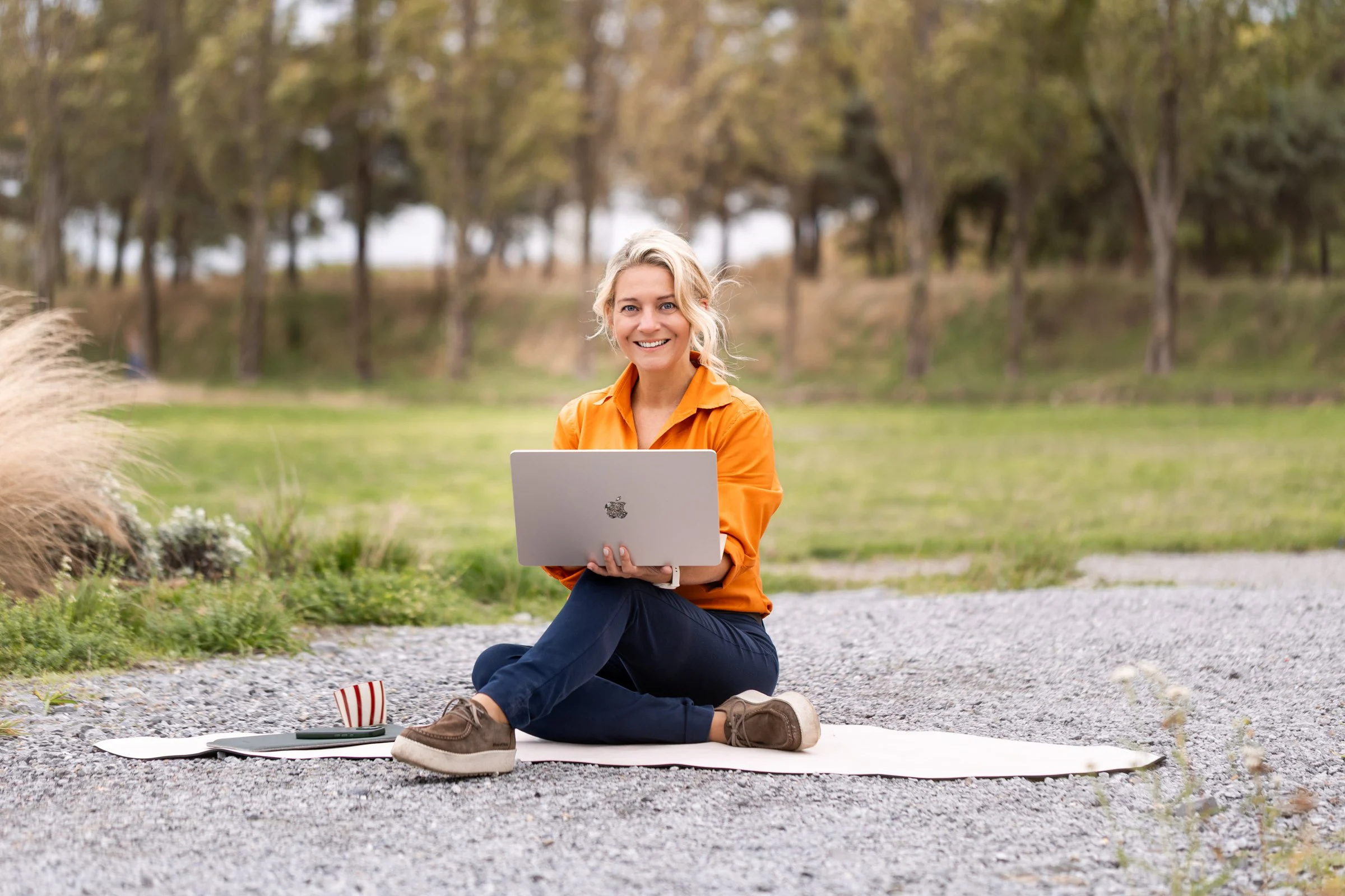 Kathrin Hörsting sitzt mit dem Laptop auf einer Matte im Grünen und lächelt in die Kamera
