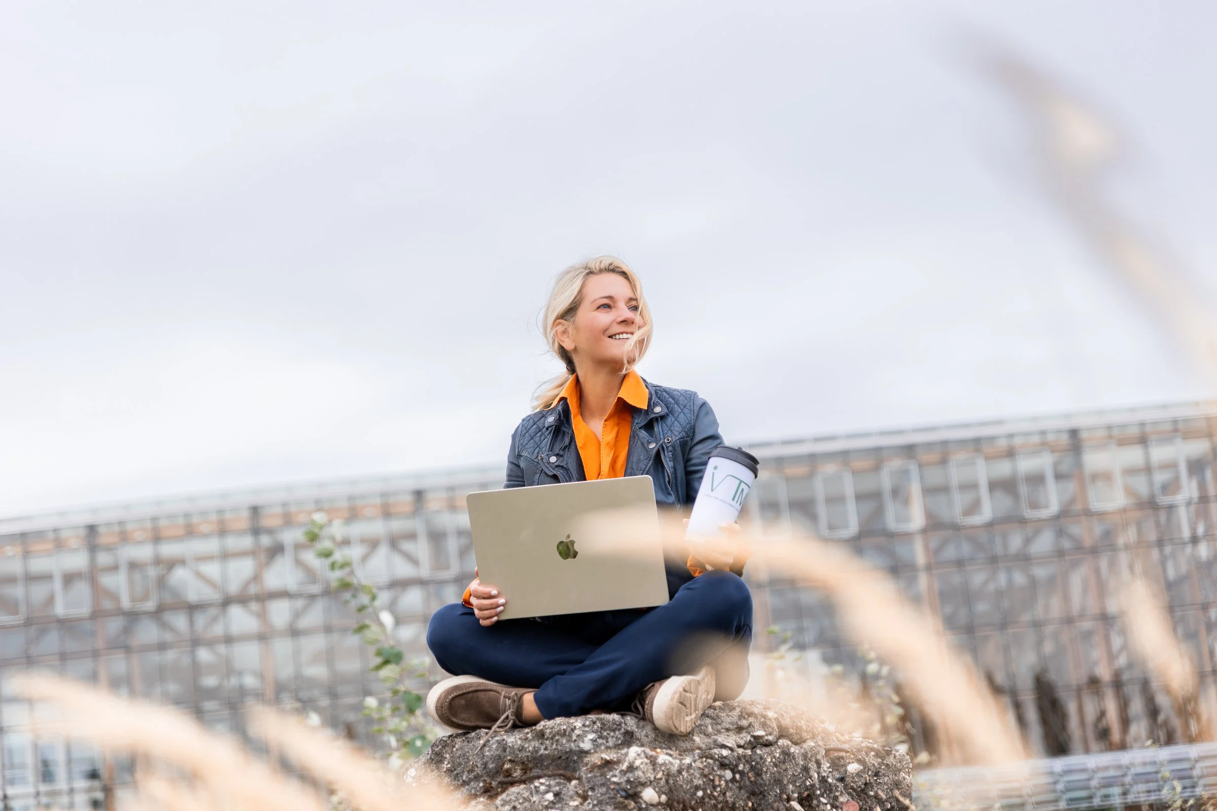 Kathrin Hörsting sitzt mit Laptop auf einem Felsen und blickt in die Ferne